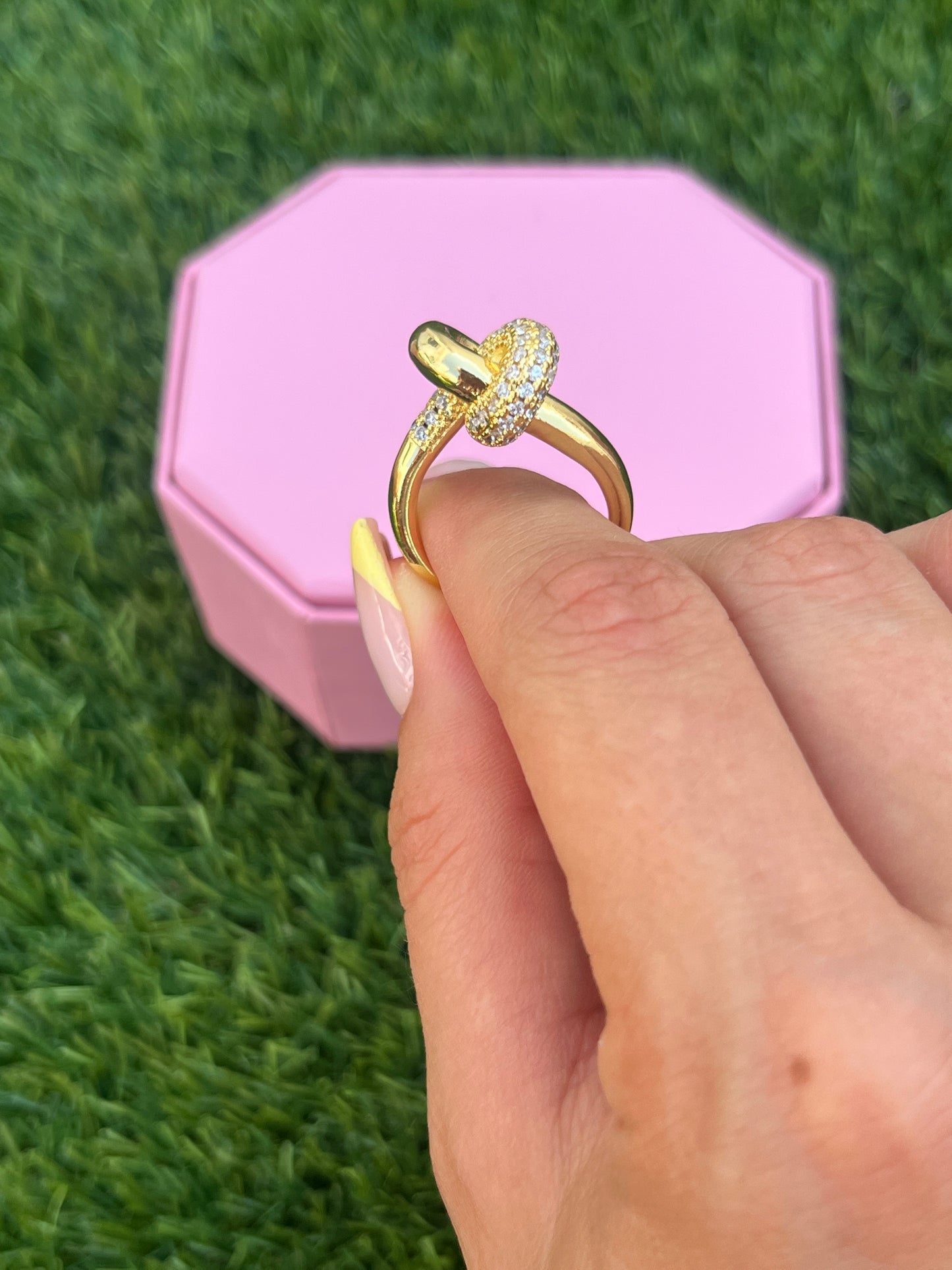 Gold knot ring on finger in grass setting, summer light