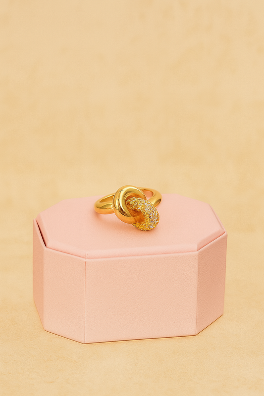 Aurora Knot Ring on soft pink pedestal with golden backdrop

