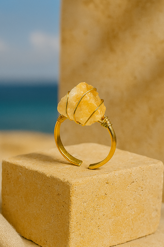 Miel Ring displayed on warm stone pedestal with ocean-blue background
